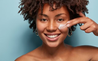 A Black woman applies facial care cream on her left cheekbone to illustrate personal care innovations with PVOH.